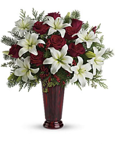 Send a touch of holiday magic to a special friend, or add some to your own home. An elegant Christmas arrangement of white asiatic lilies, red roses and Douglas fir, this fabulously fragrant gift lends seasonal sparkle to any room.
White asiatic lilies, red roses, Douglas fir, seeded eucalyptus and small red berries are gathered into a ruby red vase to create a versatile, natural piece of holiday décor.