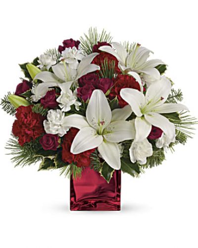 <p>Filled with holiday charm. Red spray roses and white asiatic lilies are arranged to perfection in our red mirrored cube.<br />
Red spray roses, white asiatic lilies and red carnations are accented by tips of white pine, noble fir and holly.<br />
Delivered in a beautiful red or clear cube.</p>